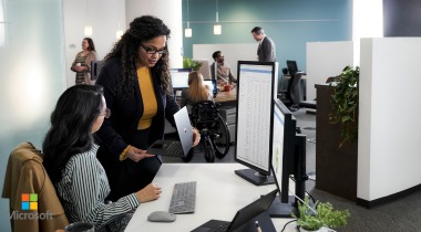 Dos mujeres trabajando frente a un computador, mientras conversan sobre algo que ven en la pantalla